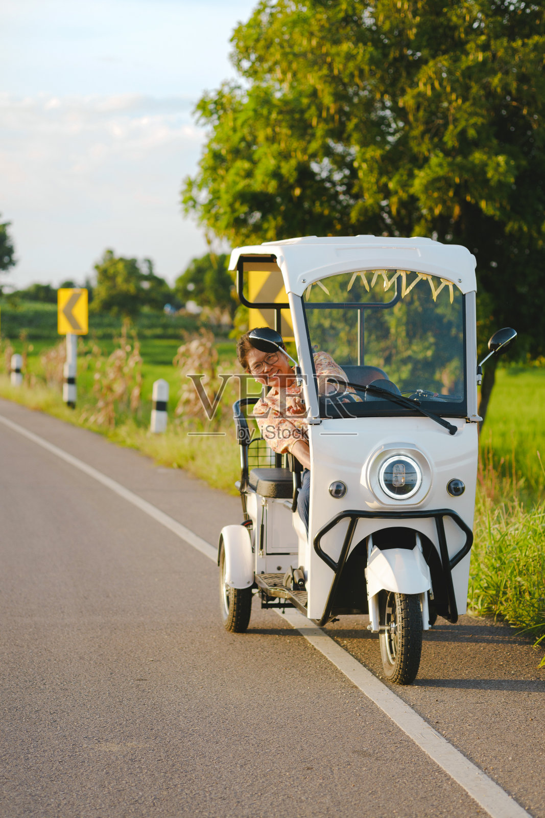 在一个阳光明媚的日子里，一位微笑的老妇人驾驶着一辆电动三轮车走在路上。照片摄影图片