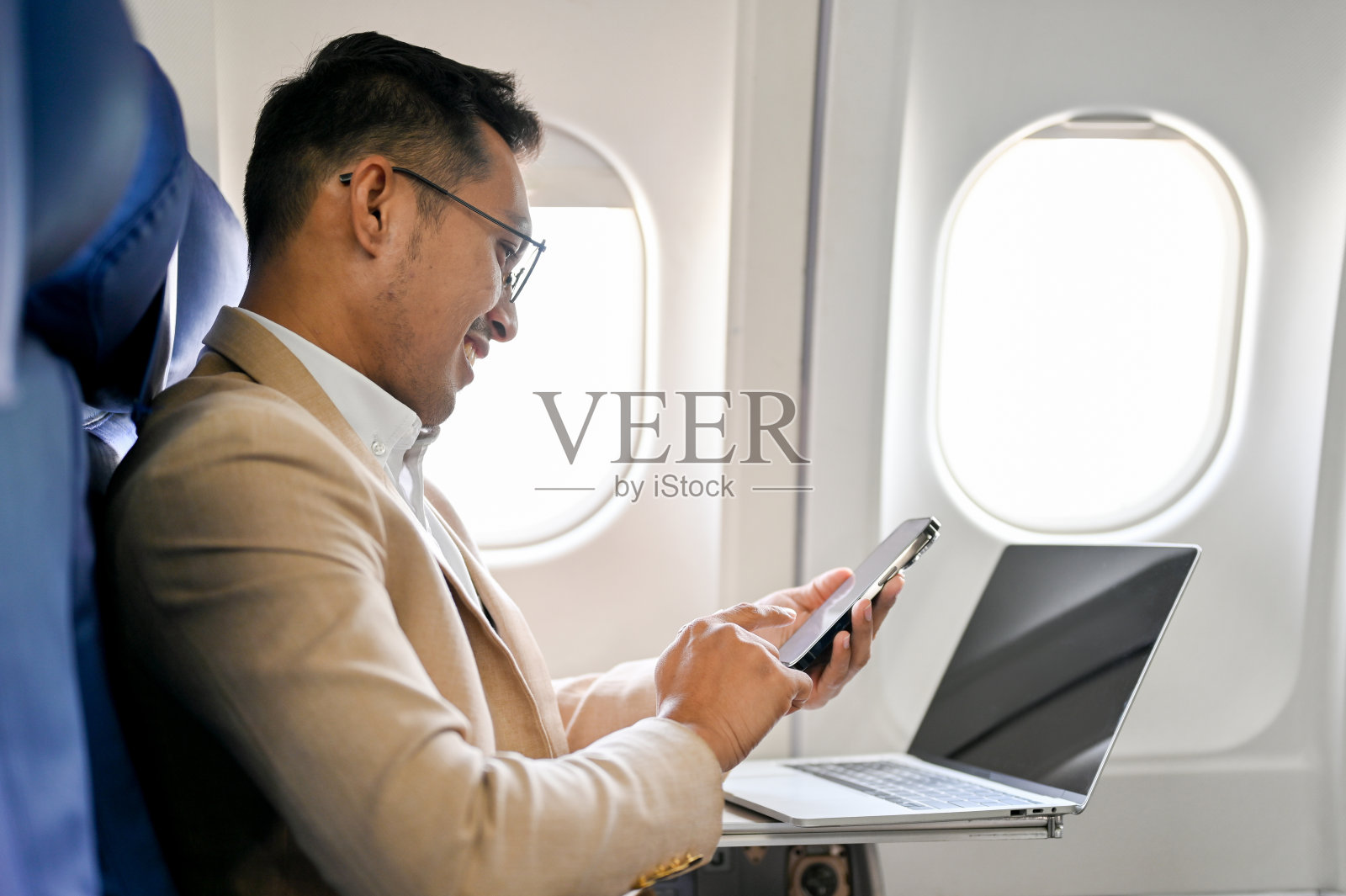 侧视图，精明的亚洲商人坐在商务舱靠窗的座位上使用智能手机照片摄影图片