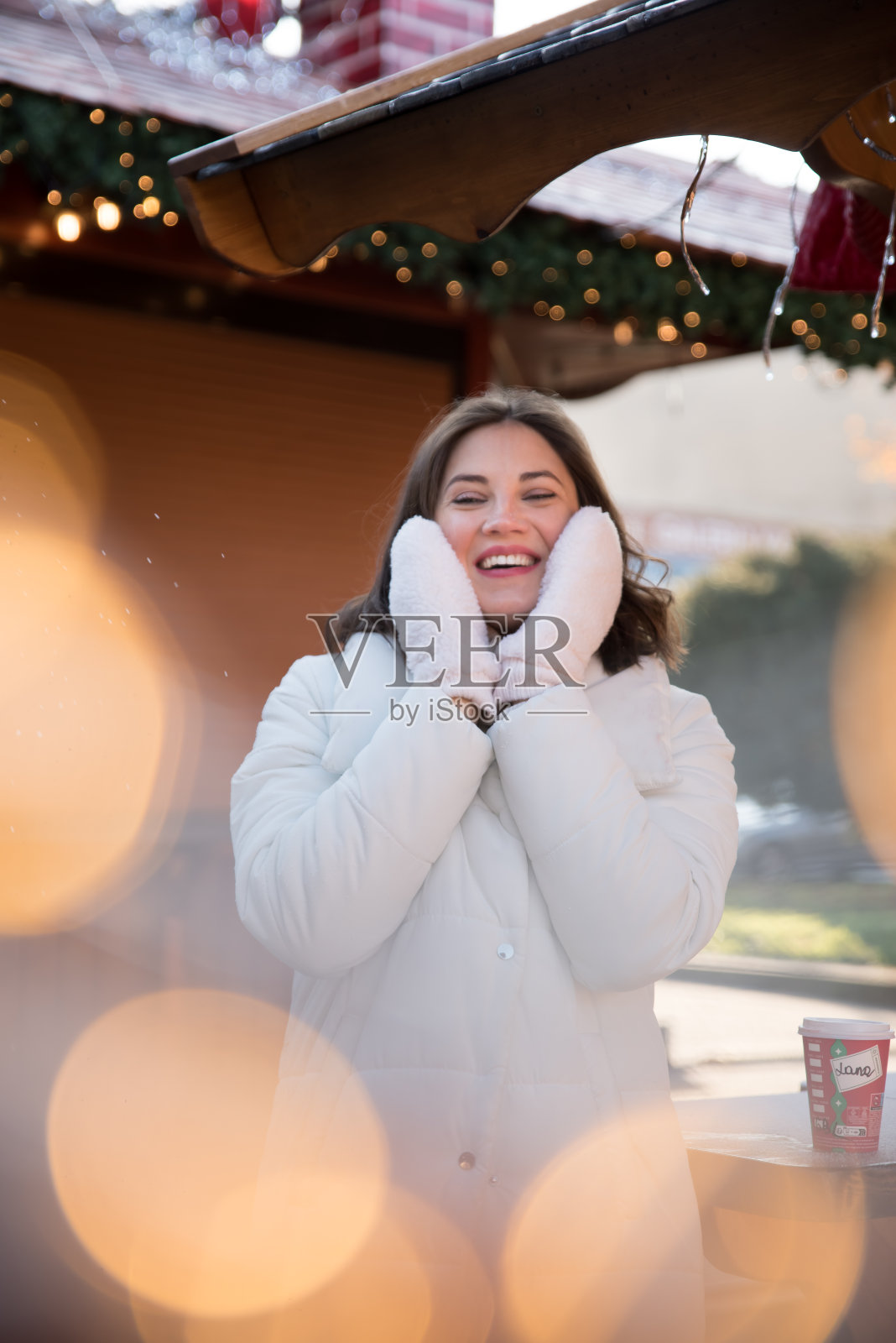 公平的。女孩穿着白夹克，戴着白帽子。女孩笑了。手里拿着一杯咖啡。木制避暑别墅。女孩喜悦。的情绪。照片摄影图片