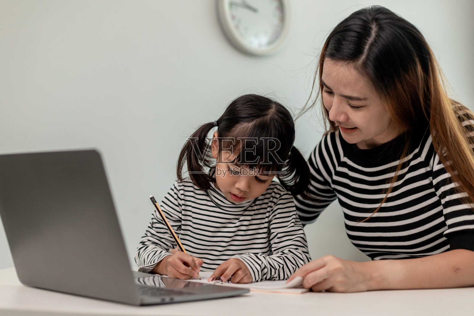 亚洲小女孩和妈妈在家学习在线课程。学龄前儿童使用笔记本电脑做作业，在妈妈的支持下，由学校老师通过数字远程互联网进行家庭教育。照片摄影图片