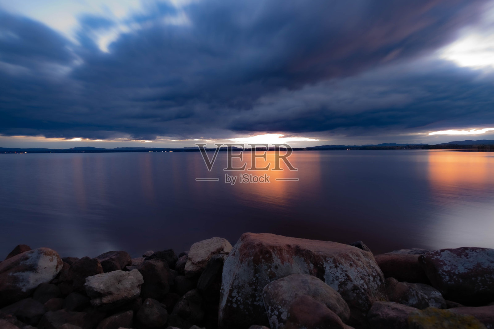 从岩石海岸捕捉到的宁静湖泊的风景，对着戏剧性的天空照片摄影图片