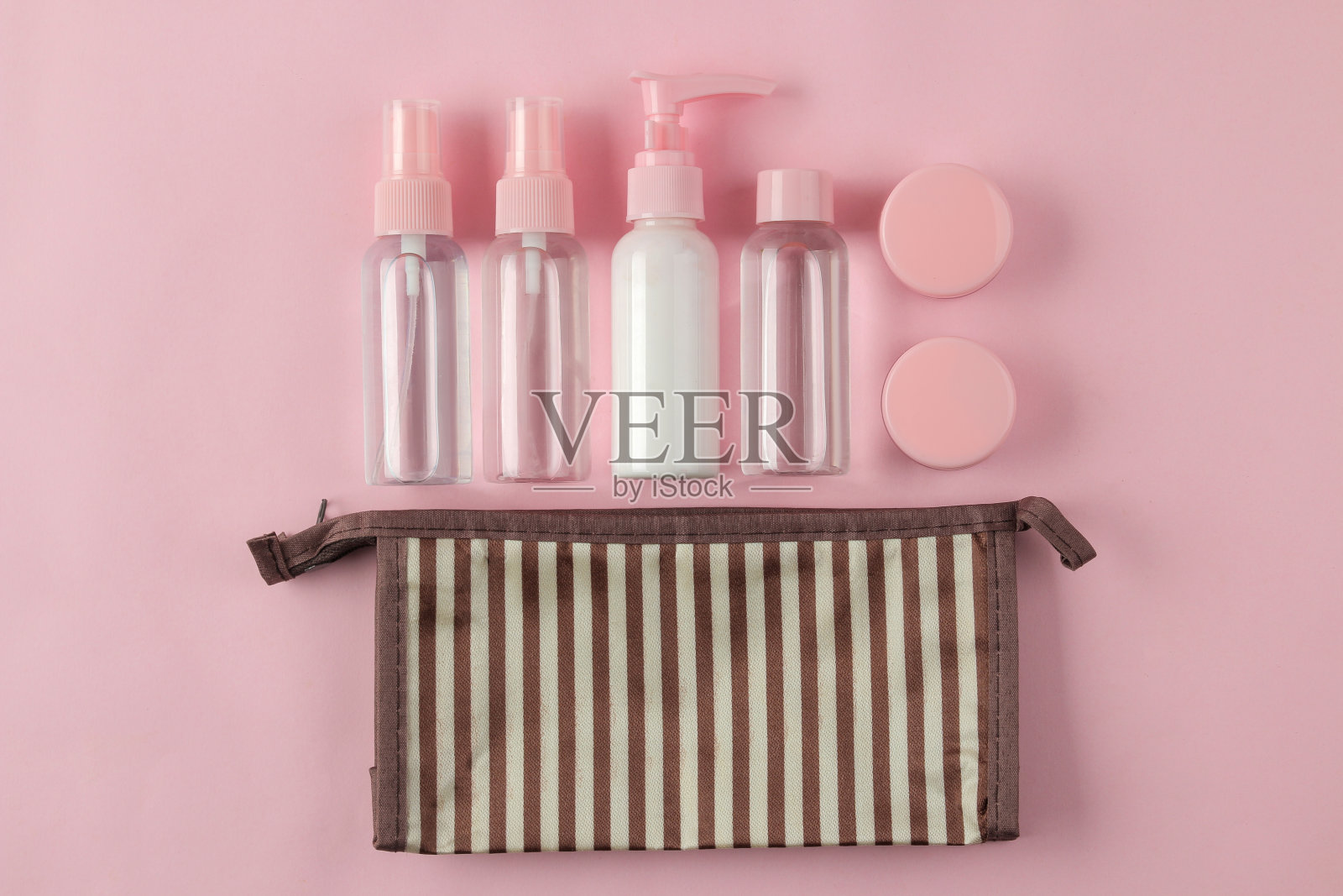 一套化妆品和个人护理产品的旅行化妆品包在浅粉色的背景。前视图。旅行的化妆品照片摄影图片