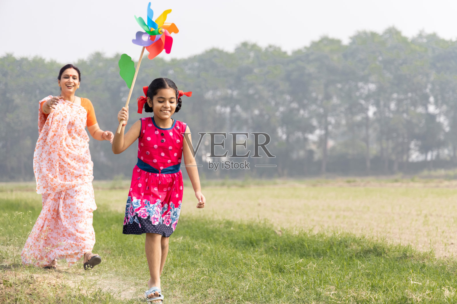 快乐的妈妈带着可爱的小女孩无忧无虑地奔跑，玩着彩色的别针轮。照片摄影图片