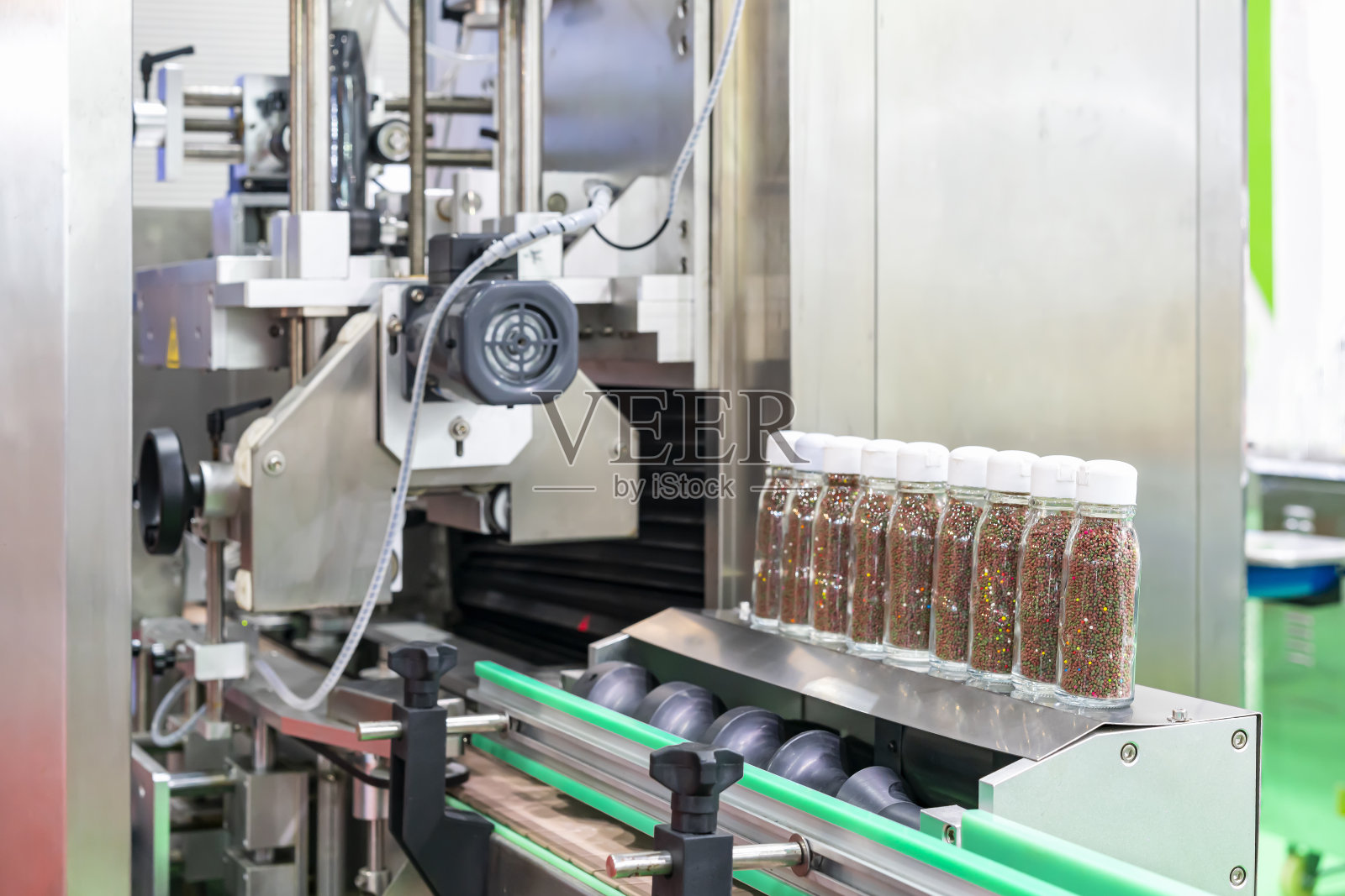 在生产过程中，小颗粒状的产品在透明瓶玻璃中被排在自动灌装封盖机上照片摄影图片