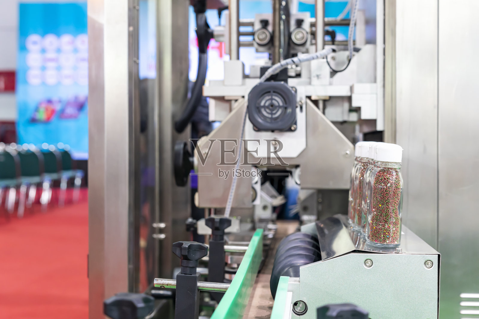 在生产过程中，小颗粒状的产品在透明瓶玻璃中被排在自动灌装封盖机上照片摄影图片