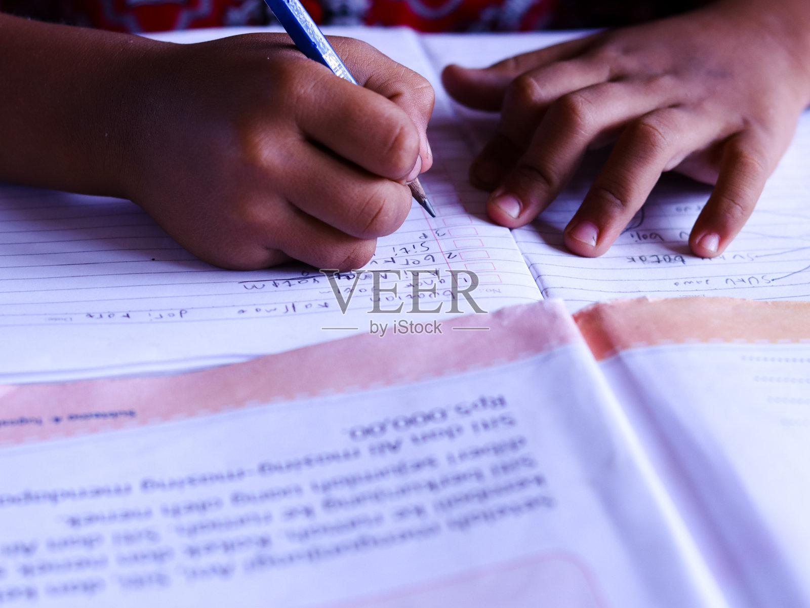 男同学在桌子上的一本书上写字。有选择性的重点。照片摄影图片