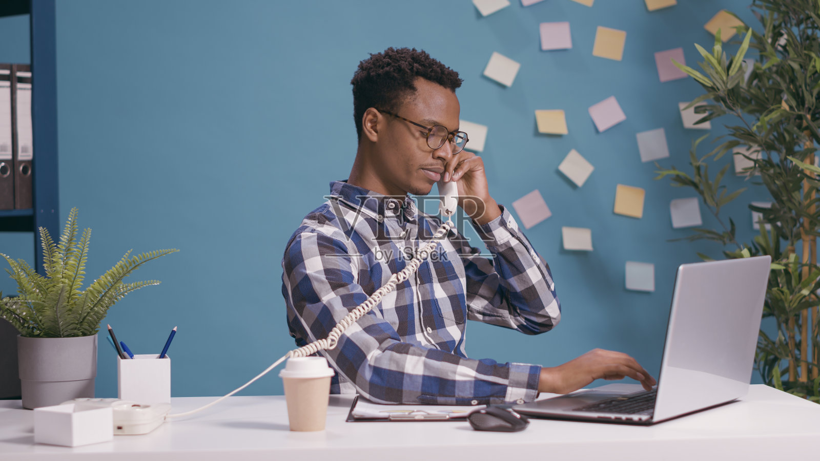 男秘书在办公桌上用笔记本电脑接听固定电话照片摄影图片