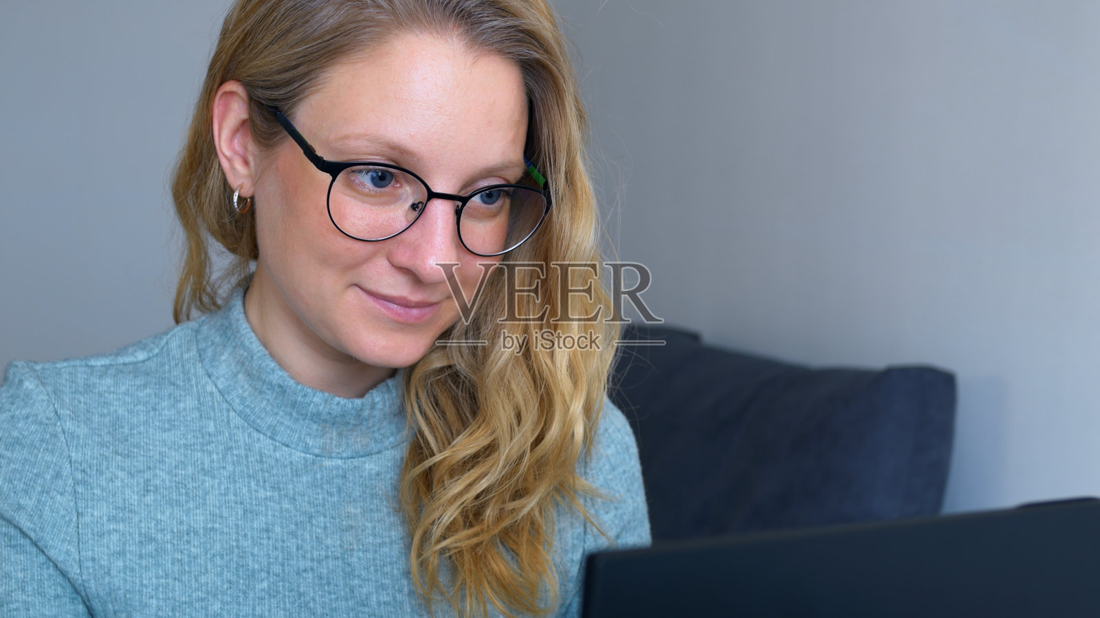 戴眼镜的年轻成功女性积极地在办公室的电脑前工作，并享受她的工作。女秘书正在她的工作场所用笔记本电脑打字。女人把她的金发藏在耳朵后面。照片摄影图片