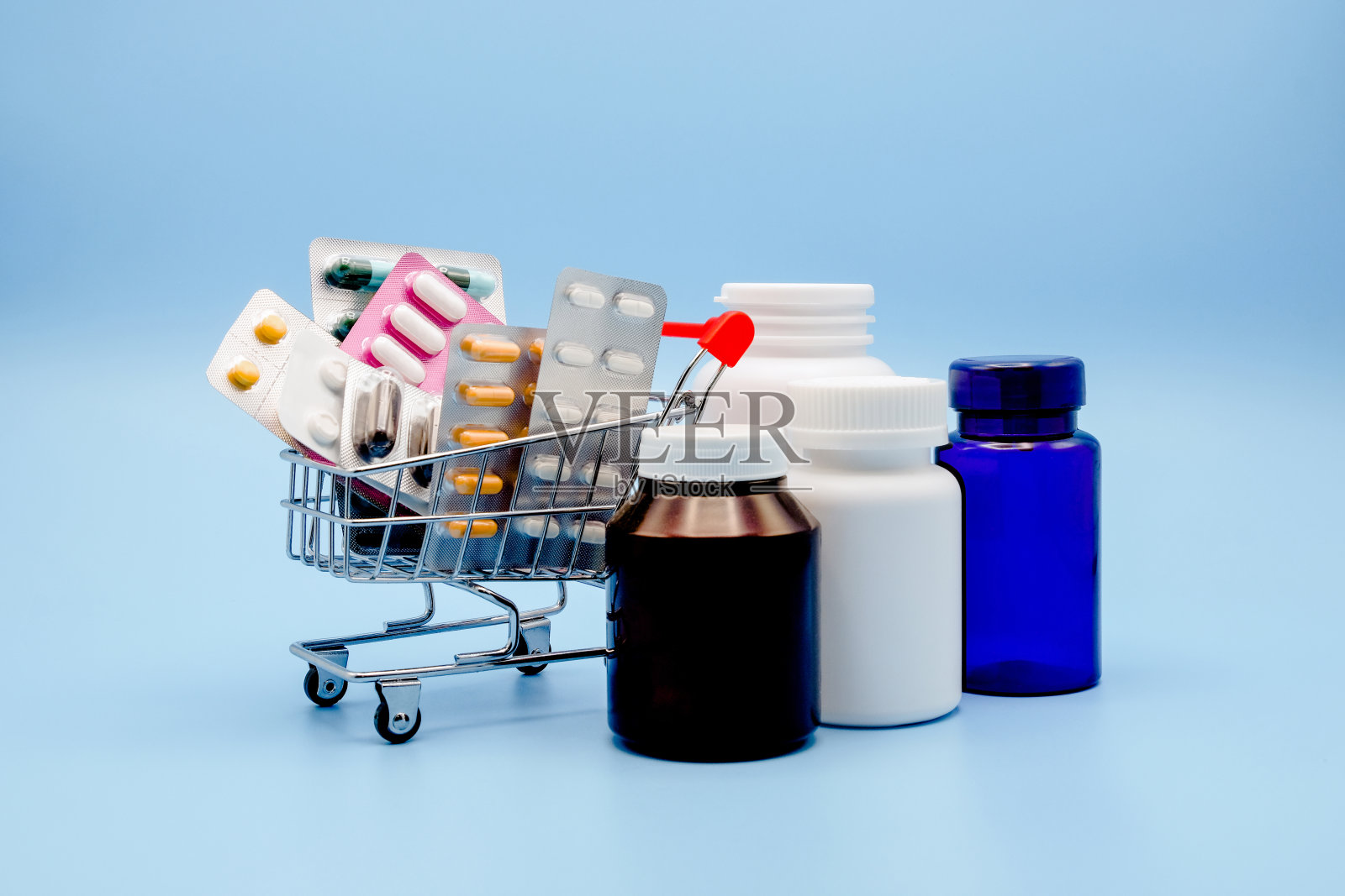 医学概念。各种胶囊，一包药物在购物车与药瓶在一个蓝色的背景。药的概念。购买药品。照片摄影图片