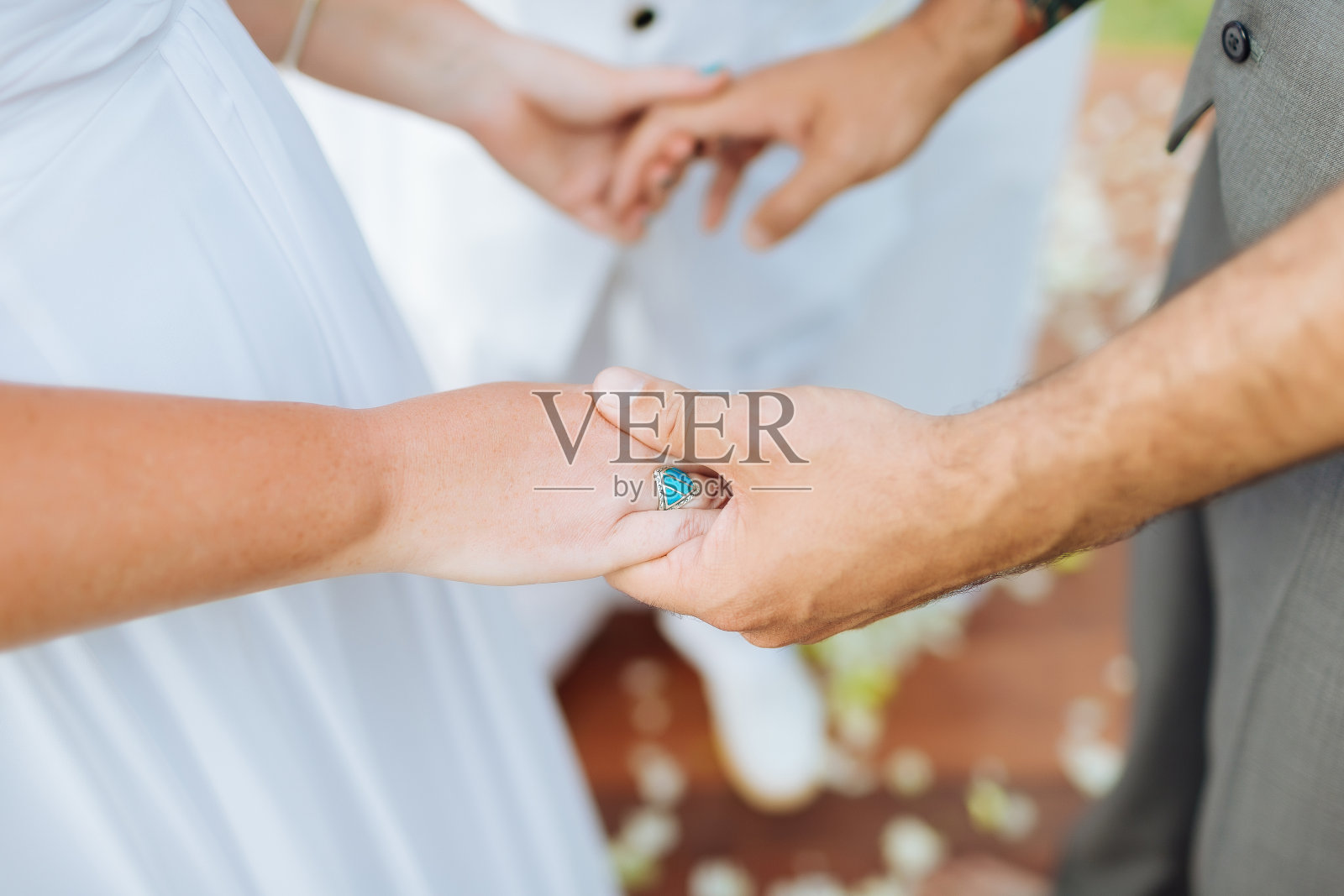 新娘和新郎在婚礼上手牵着手的照片。新娘在一个地方戴了一枚漂亮的蓝色订婚戒指。有一位牧师站在那里作证。照片摄影图片