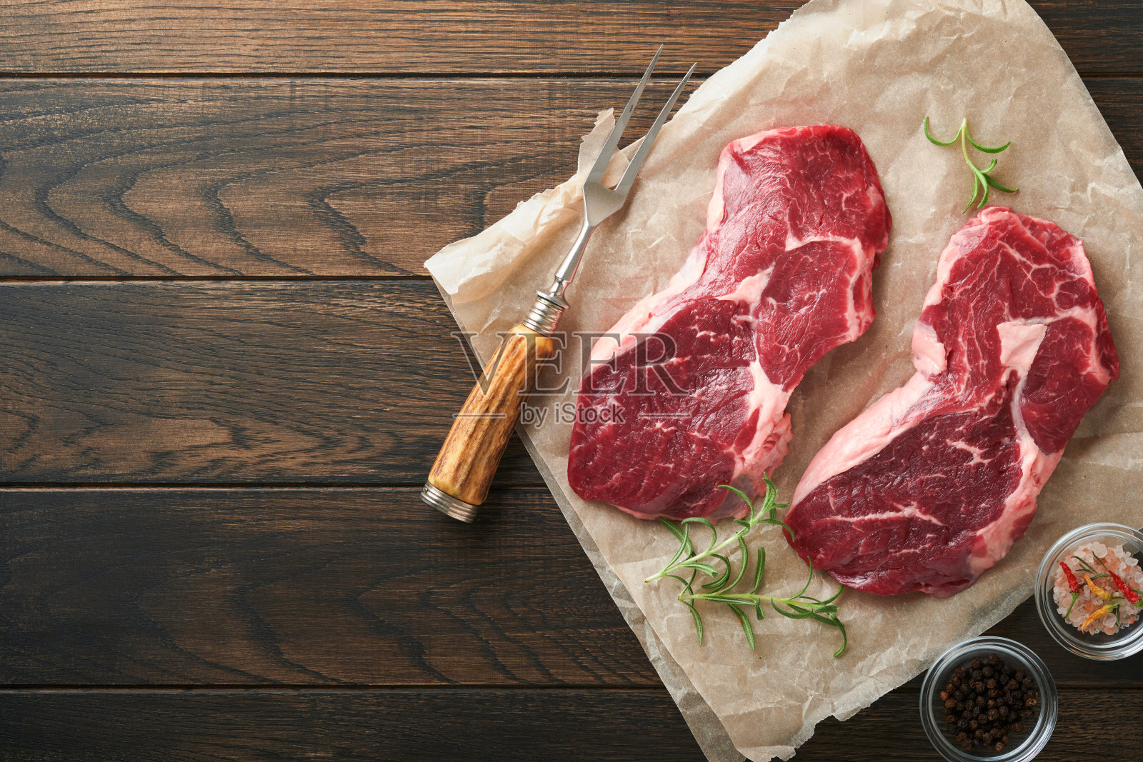 生牛排。大理石生新鲜肋眼牛排与迷迭香，盐和胡椒在砧板上的深色混凝土背景。生牛排和烹饪用香料。照片摄影图片