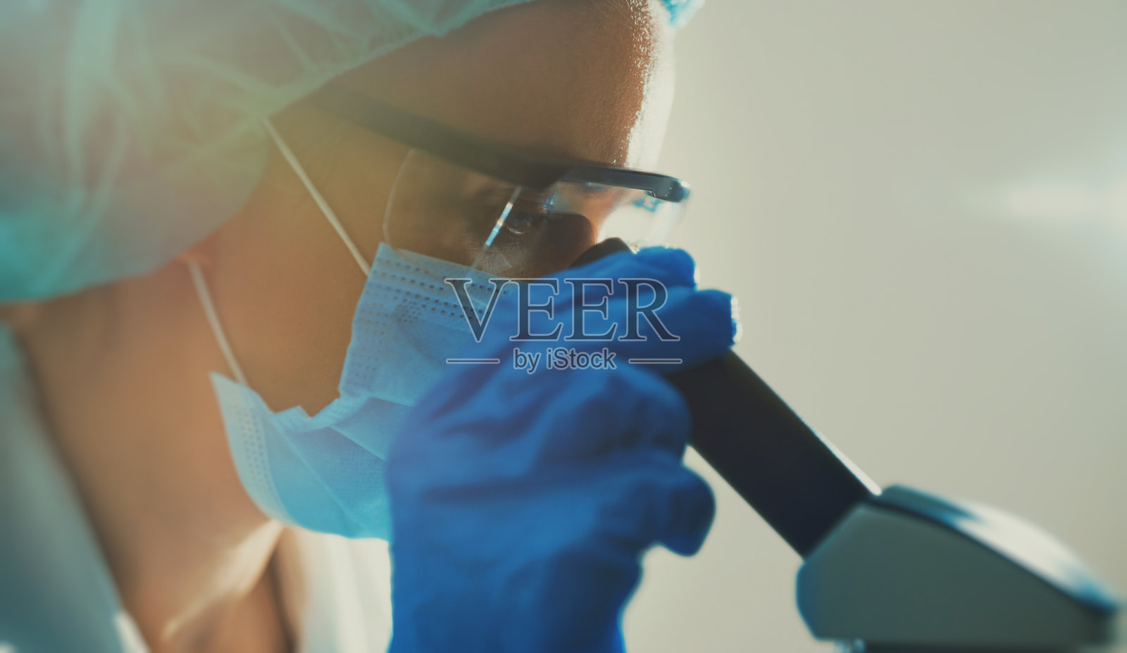 科学家戴着医用口罩在实验室用显微镜工作。照片摄影图片