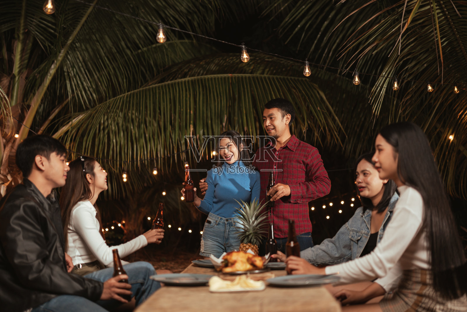 亚洲夫妇与团体朋友庆祝周年晚宴。在夜晚的灯光下，和朋友一起享受幸福的情侣晚餐。照片摄影图片