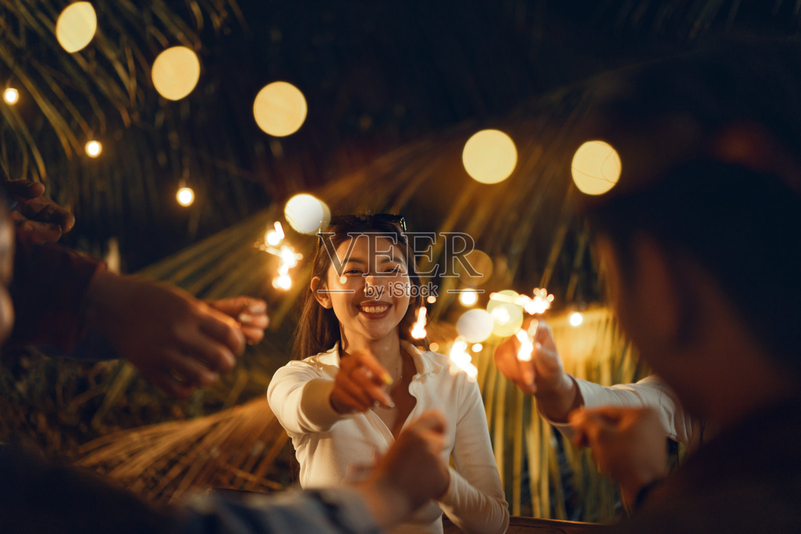 快乐的亚洲妇女与她的朋友们在户外庆祝节日的晚会上玩烟花。照片摄影图片