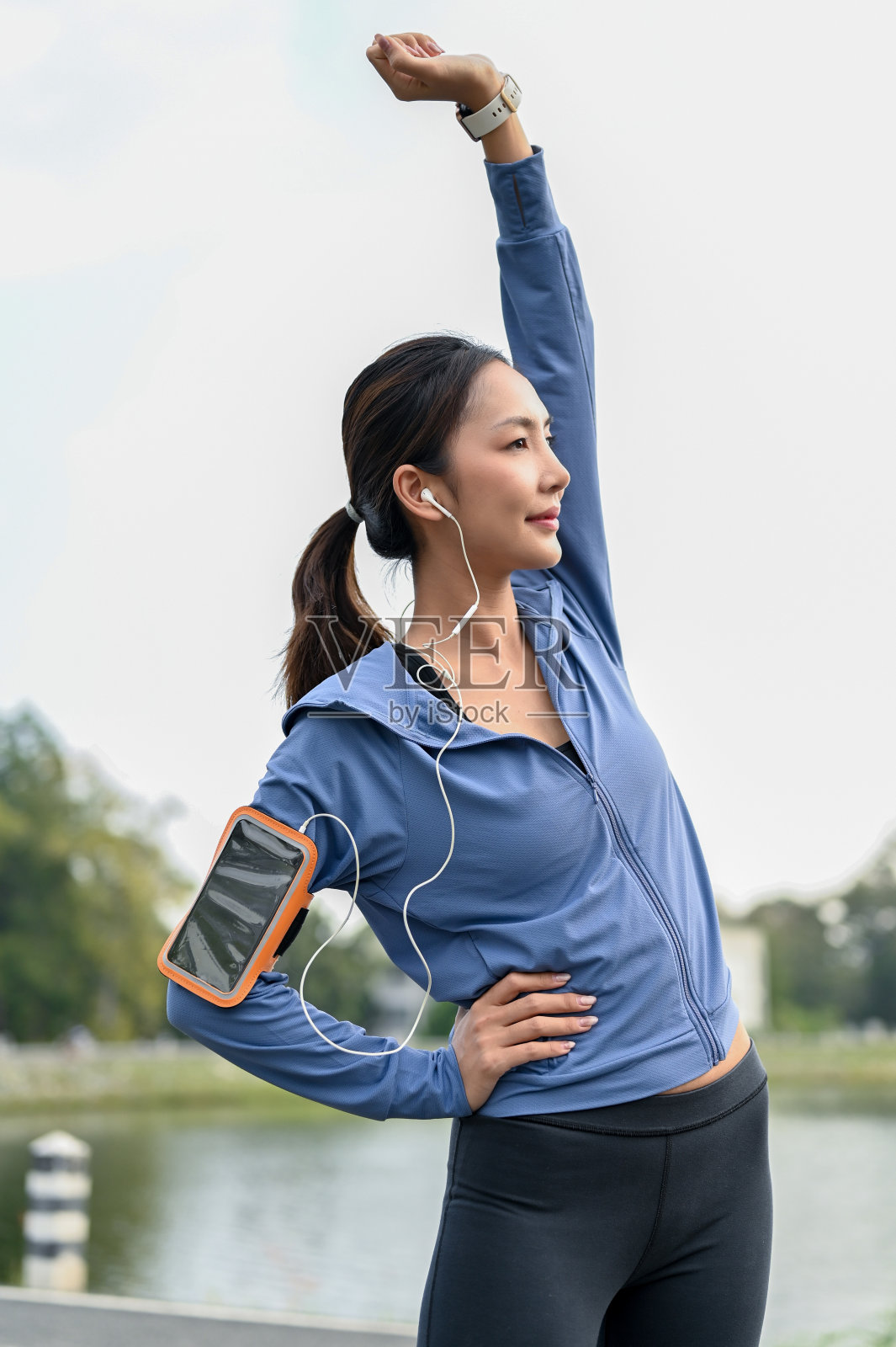 活跃的亚洲女性在伸展双臂时通过耳机听音乐。照片摄影图片