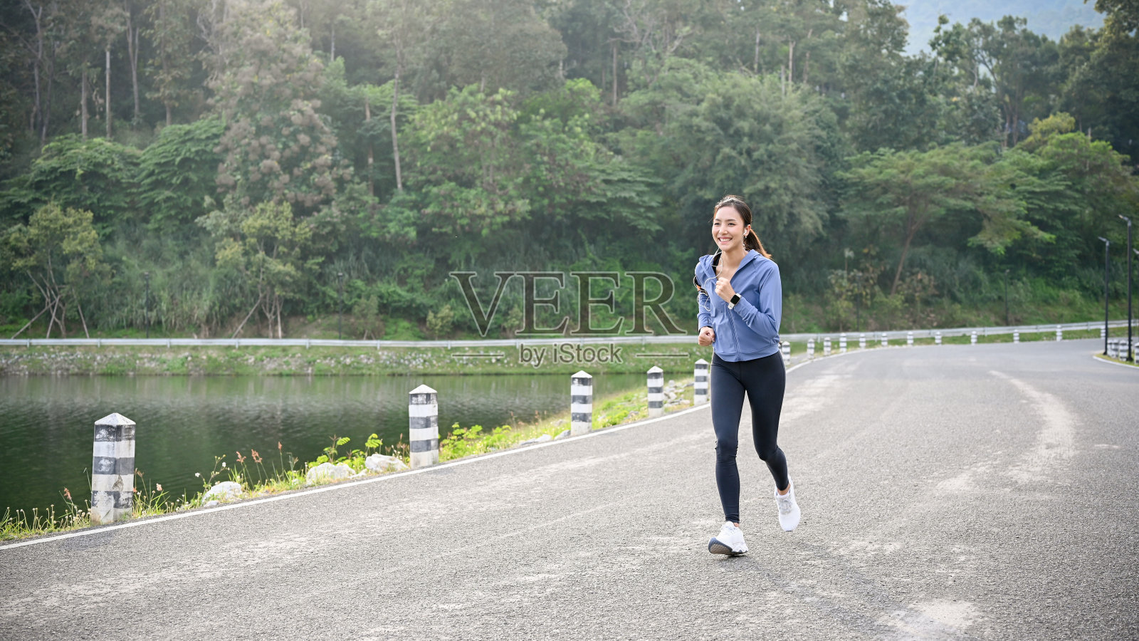 快乐的亚洲女人在积极的运动服听音乐，沿着街道奔跑。照片摄影图片