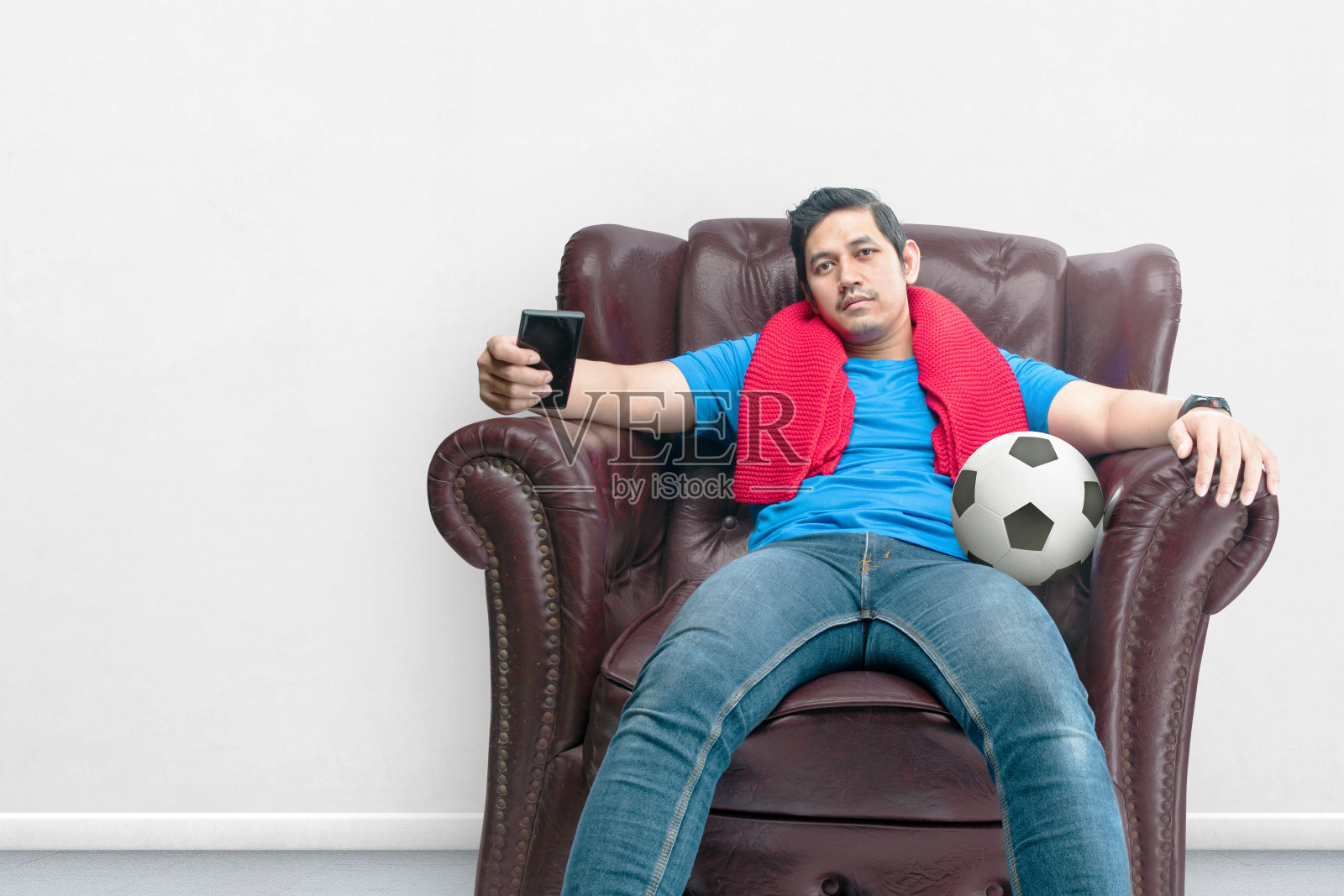 一个带着围巾和球的亚洲男人带着失望的表情坐在沙发上看足球照片摄影图片
