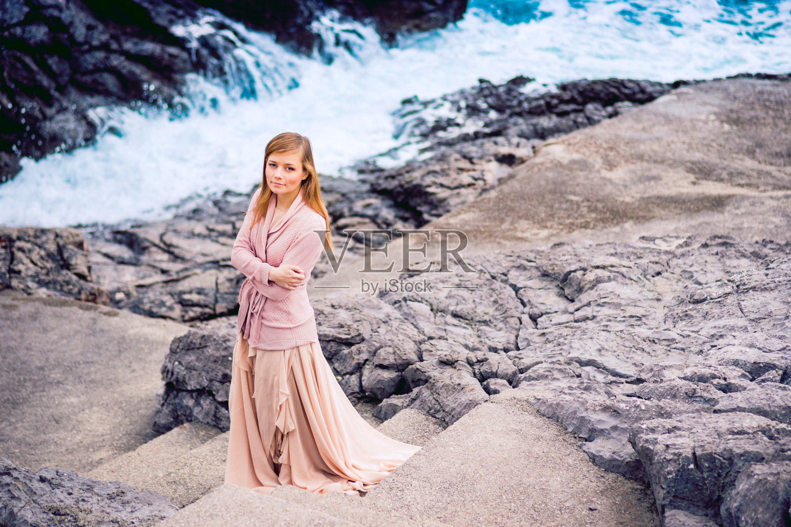 在黑山布德瓦海岸的亚得里亚海附近，一名女子穿着美丽的玫瑰裙。水，岩石和山。照片摄影图片