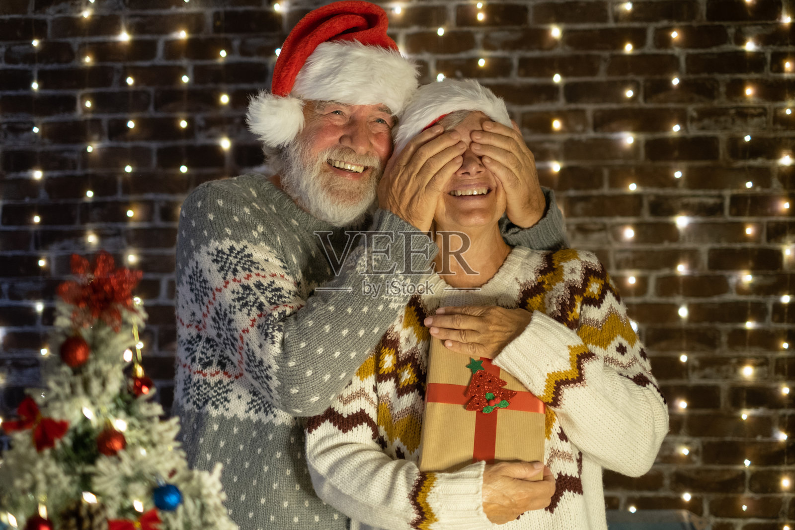 给她个惊喜。圣诞节活动和庆祝活动。戴着圣诞老人帽子的快乐老人夫妇交换礼物照片摄影图片