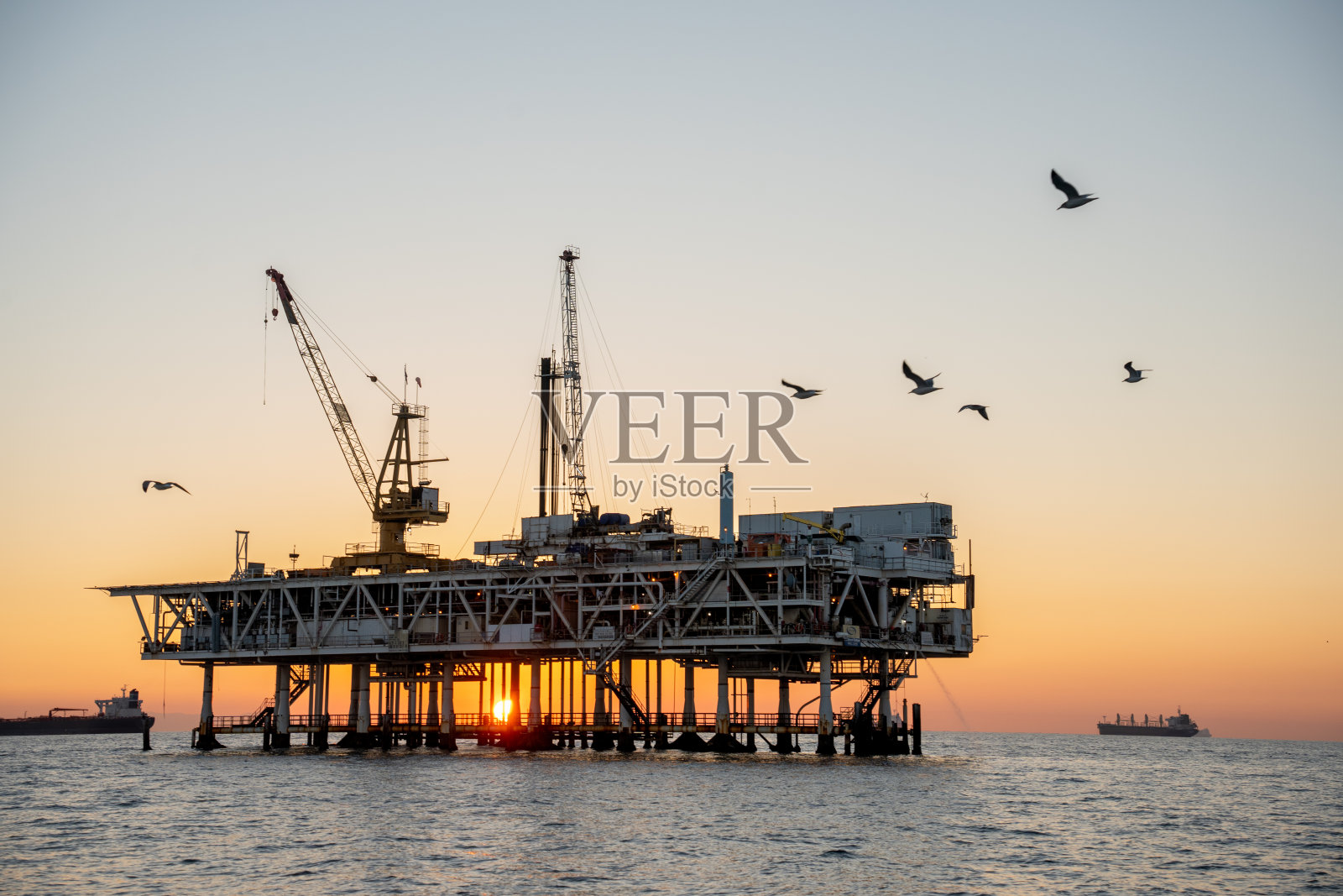 近海钻井平台与长滩和洛杉矶加州在黄昏与海鸥在前景飞行的背景照片摄影图片