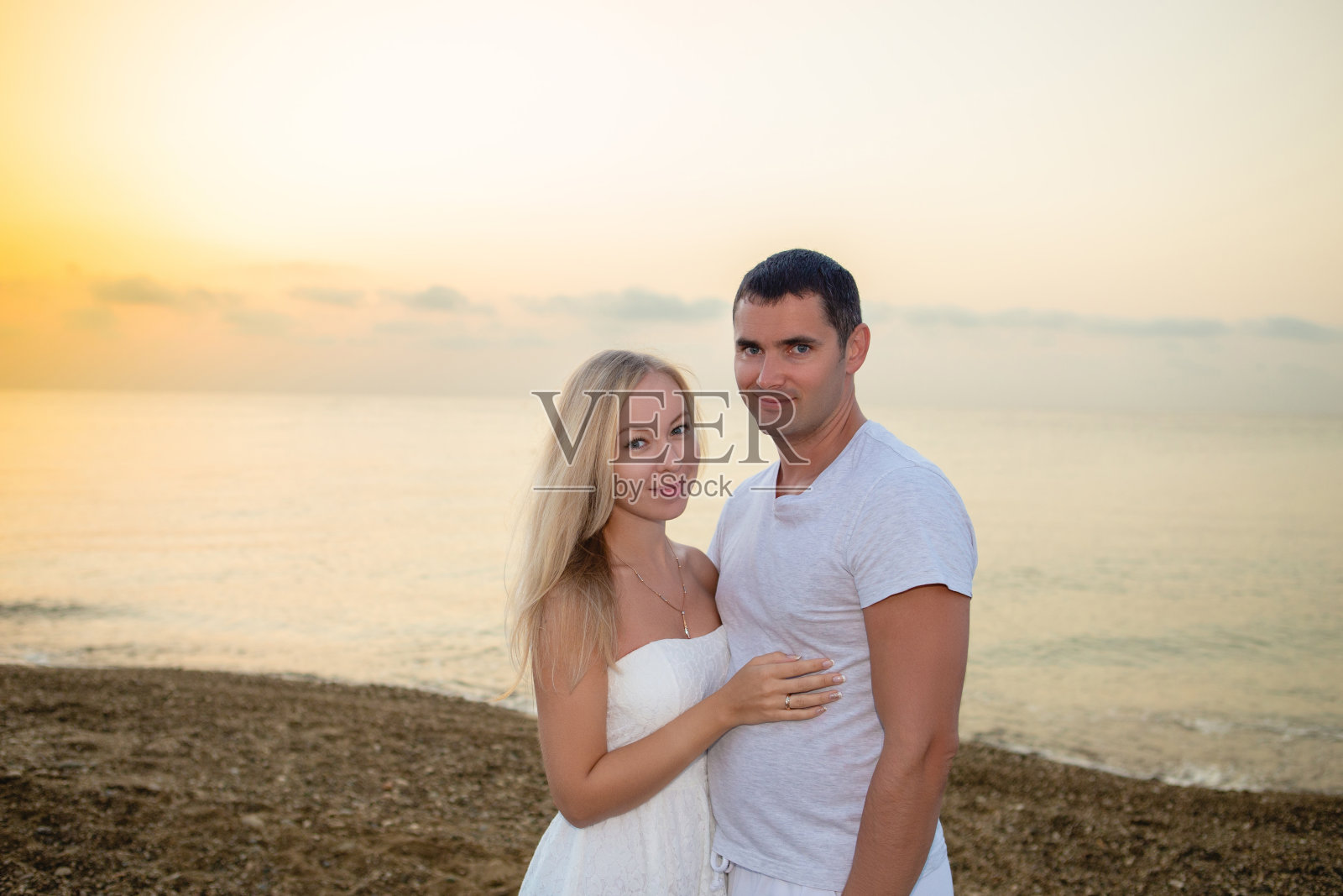 年轻的情侣在海边的日落或日出的背景。照片摄影图片