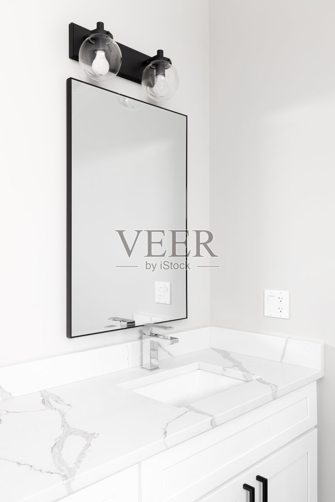 浴室里有白色的橱柜和水槽，有黑色的灯和镜子。照片摄影图片