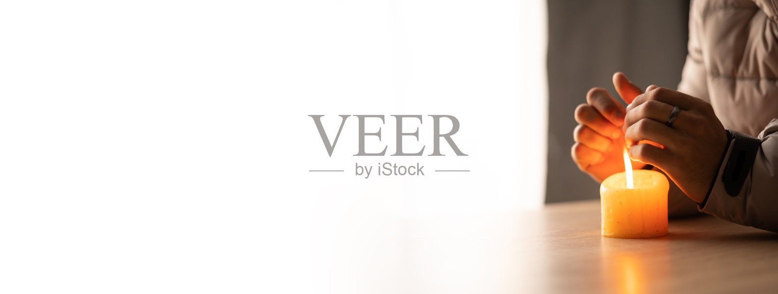 年轻人穿着暖和的衣服坐在桌子旁，烛光温暖着他。关闭暖气、电力、停电、断电、断电或能源危机，无电、无暖气照片摄影图片