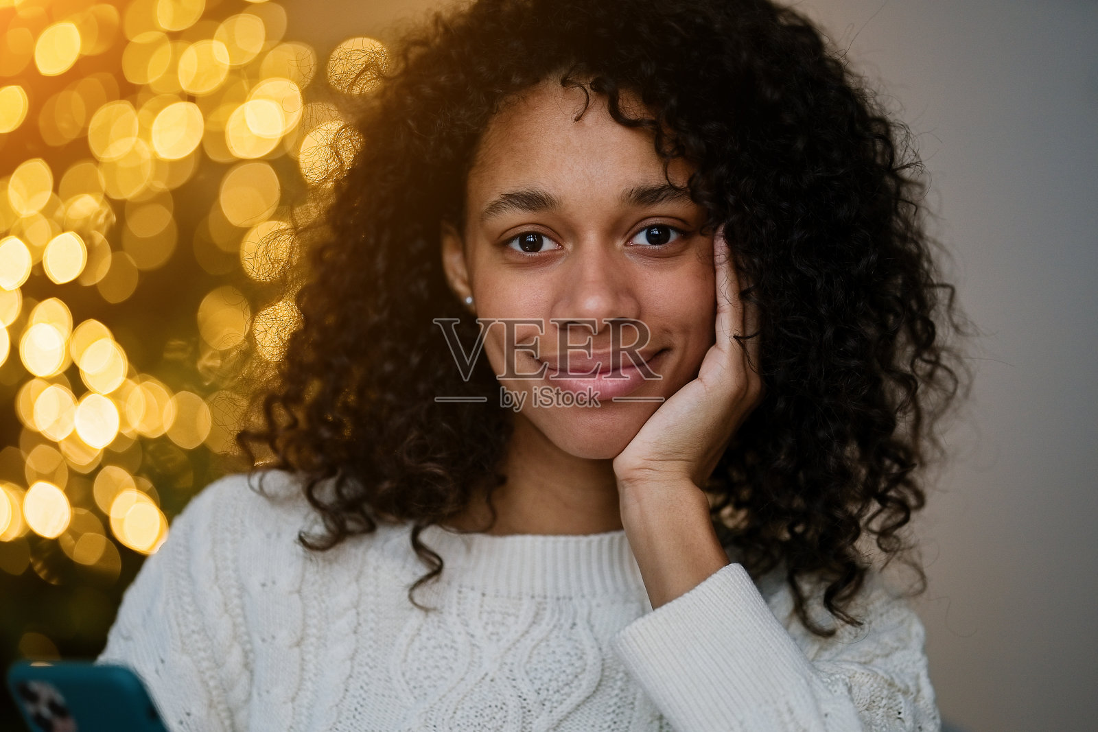 一名非裔美国妇女在舒适的客厅的圣诞树旁用智能手机聊天照片摄影图片