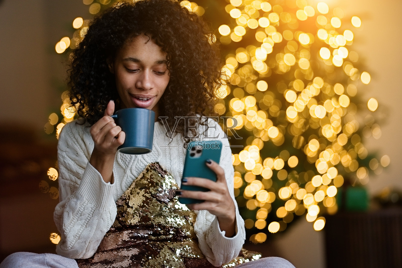 年轻的非裔美国妇女在圣诞树旁用智能手机聊天照片摄影图片