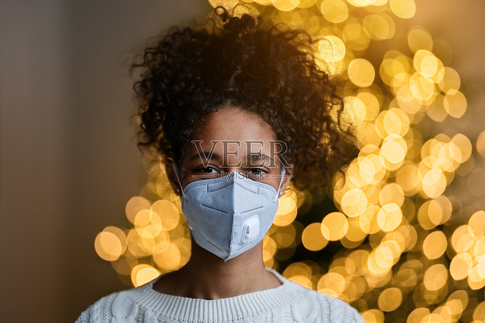 肖像年轻的非裔美国妇女在戴口罩在圣诞树上在舒适的客厅照片摄影图片