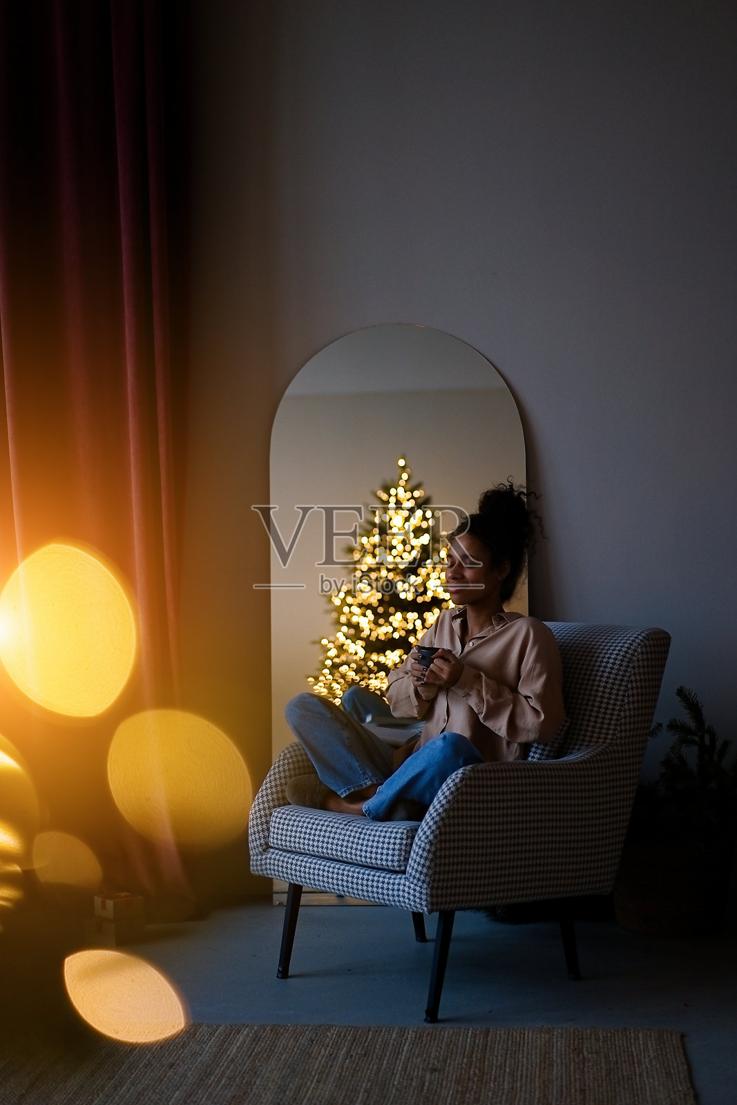 年轻的非裔美国妇女坐在扶手椅上，在圣诞树旁喝咖啡照片摄影图片