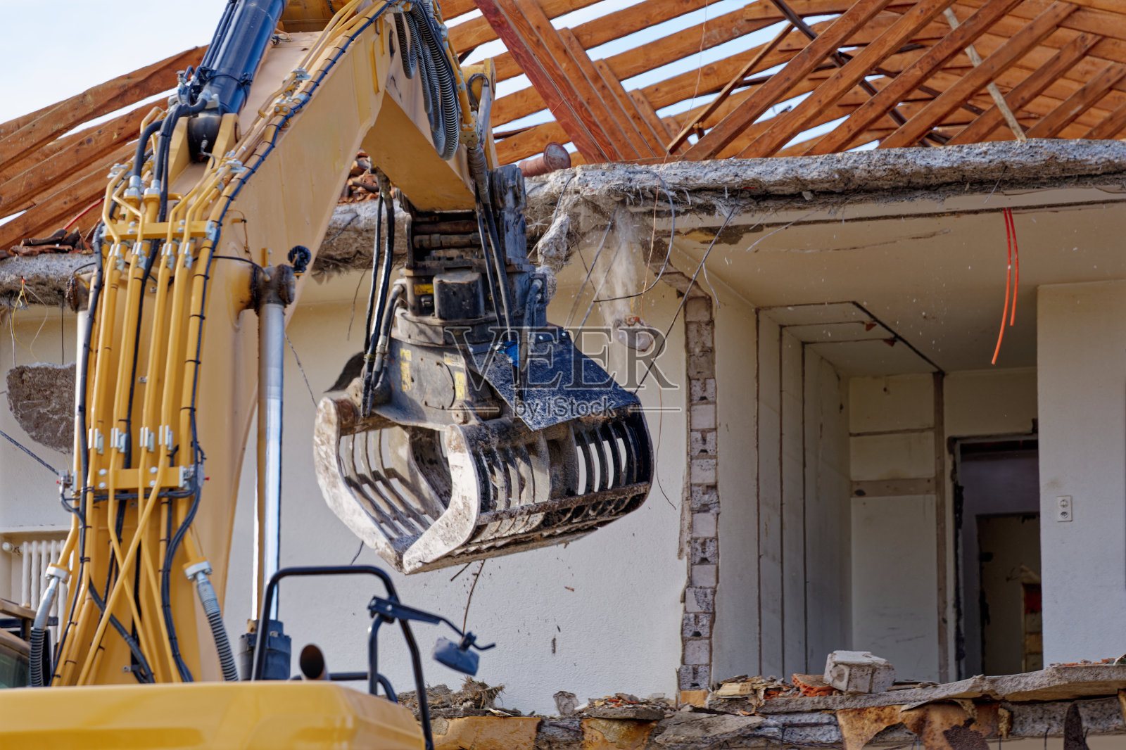 在一个阳光明媚的秋日，挖掘机用黑爪拆除了一座带有木质屋顶框架的公寓楼。照片摄影图片