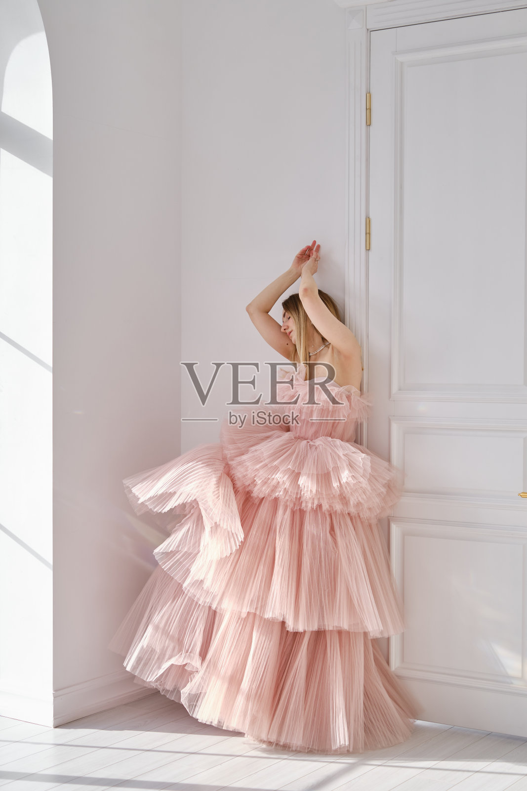 一个女孩站在一堵浅色的墙边，她穿着一件灰蒙蒙的玫瑰色的美丽茂盛的长裙。复古的新娘魅力。穿着婚纱或晚礼服拍摄时装照片摄影图片