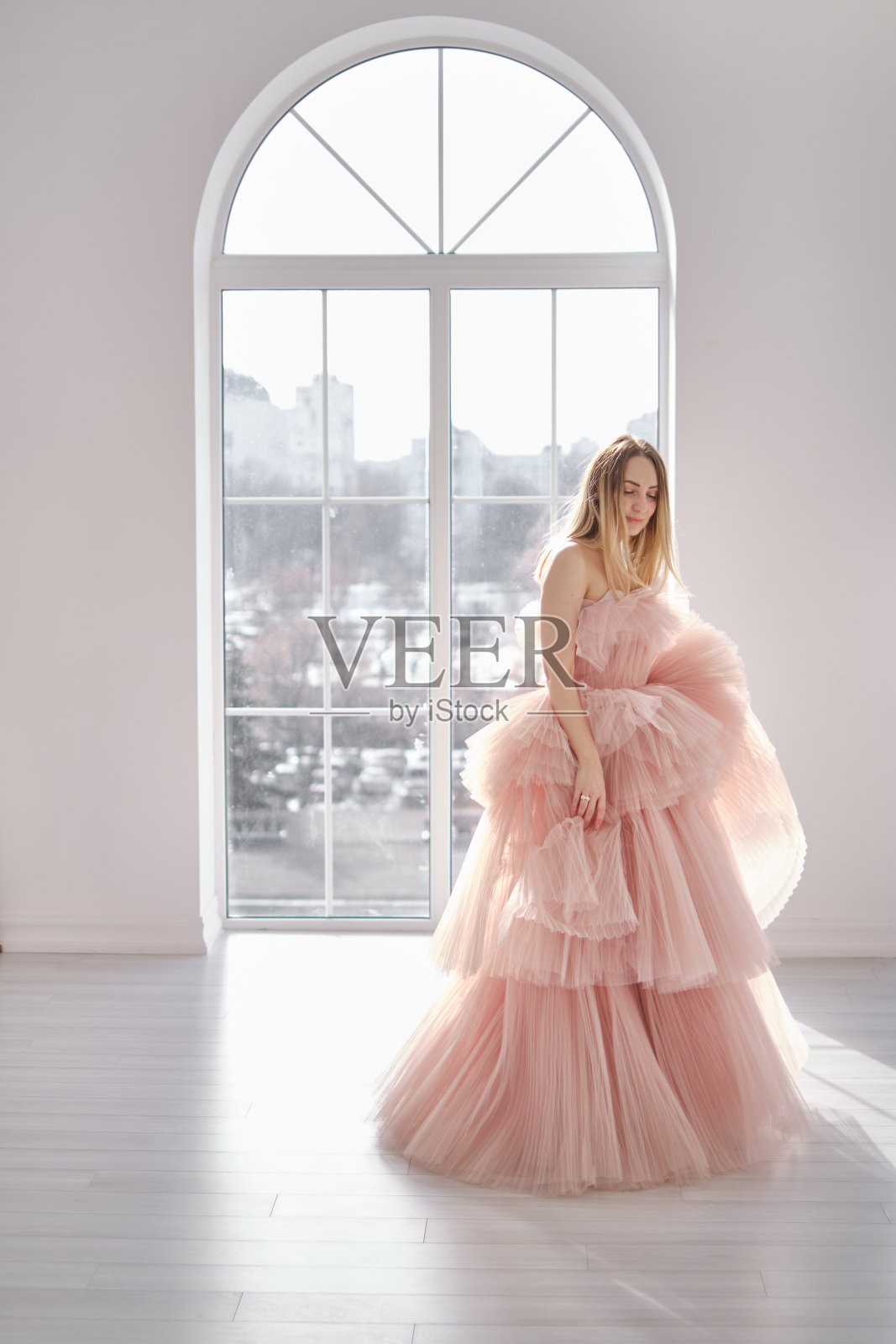 一个女孩站在一扇开着的窗户旁，她穿着一件美丽而华丽的灰玫瑰色长裙。复古的新娘魅力。穿着婚纱或晚礼服拍摄时装照片摄影图片