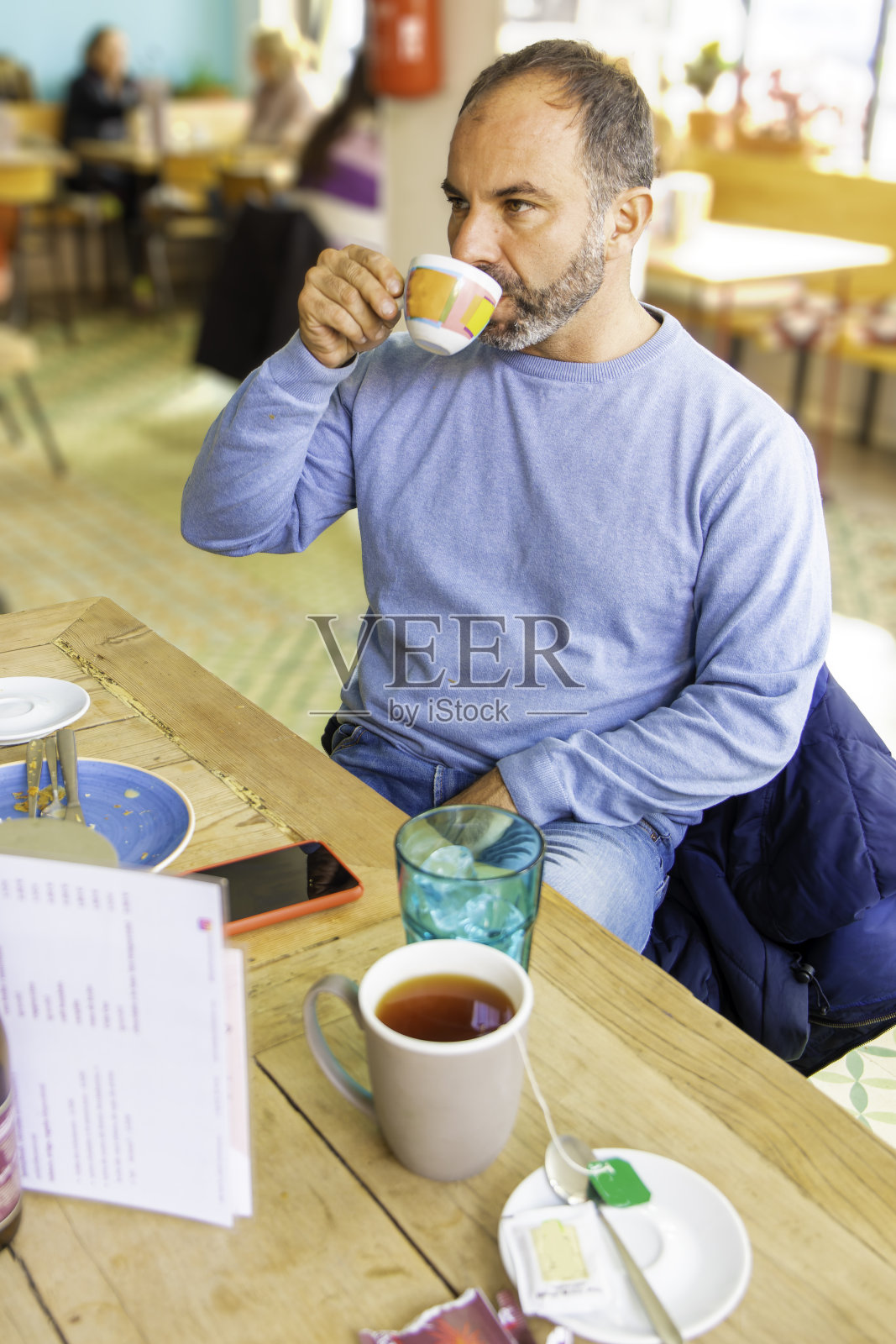 一名留着胡子的成年男子在一家现代自助餐厅用彩色咖啡杯喝咖啡照片摄影图片
