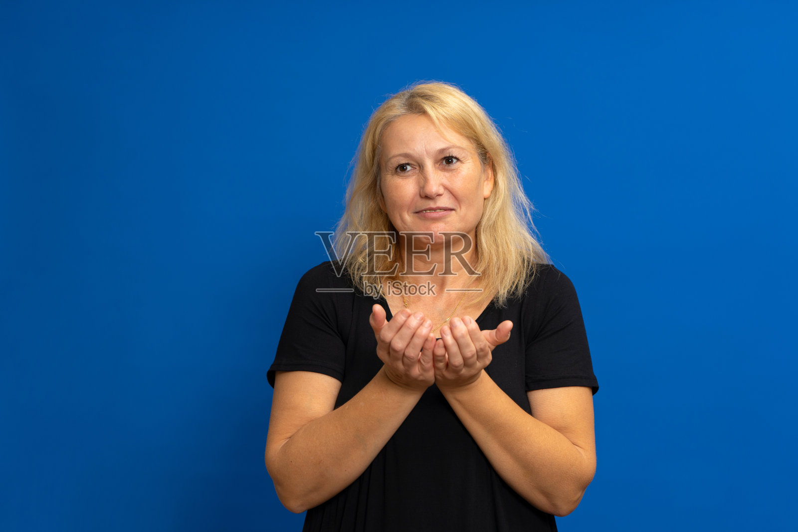 一个微笑的特写肖像，快乐兴奋的美丽女子举起手掌，在你提供一些东西，孤立在蓝色背景。积极情绪，面部表情，符号符号。照片摄影图片