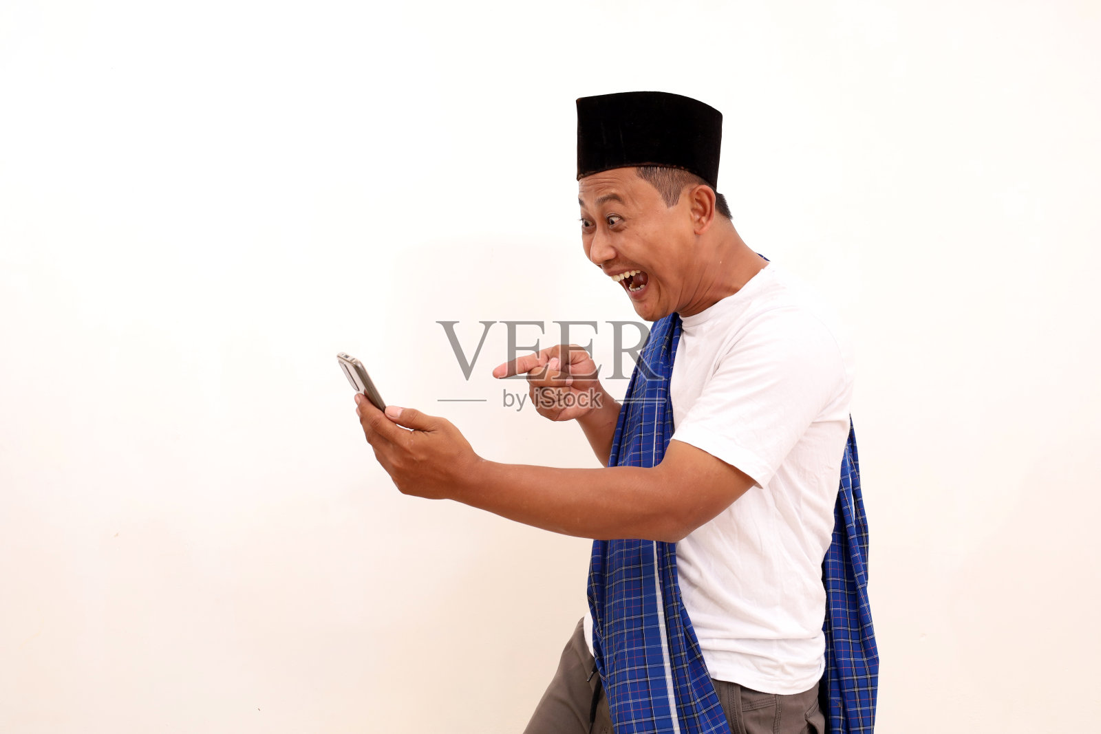 快乐的亚洲男人的肖像，站着，拿着，指着手机。孤立在白色上。斋月的概念照片摄影图片