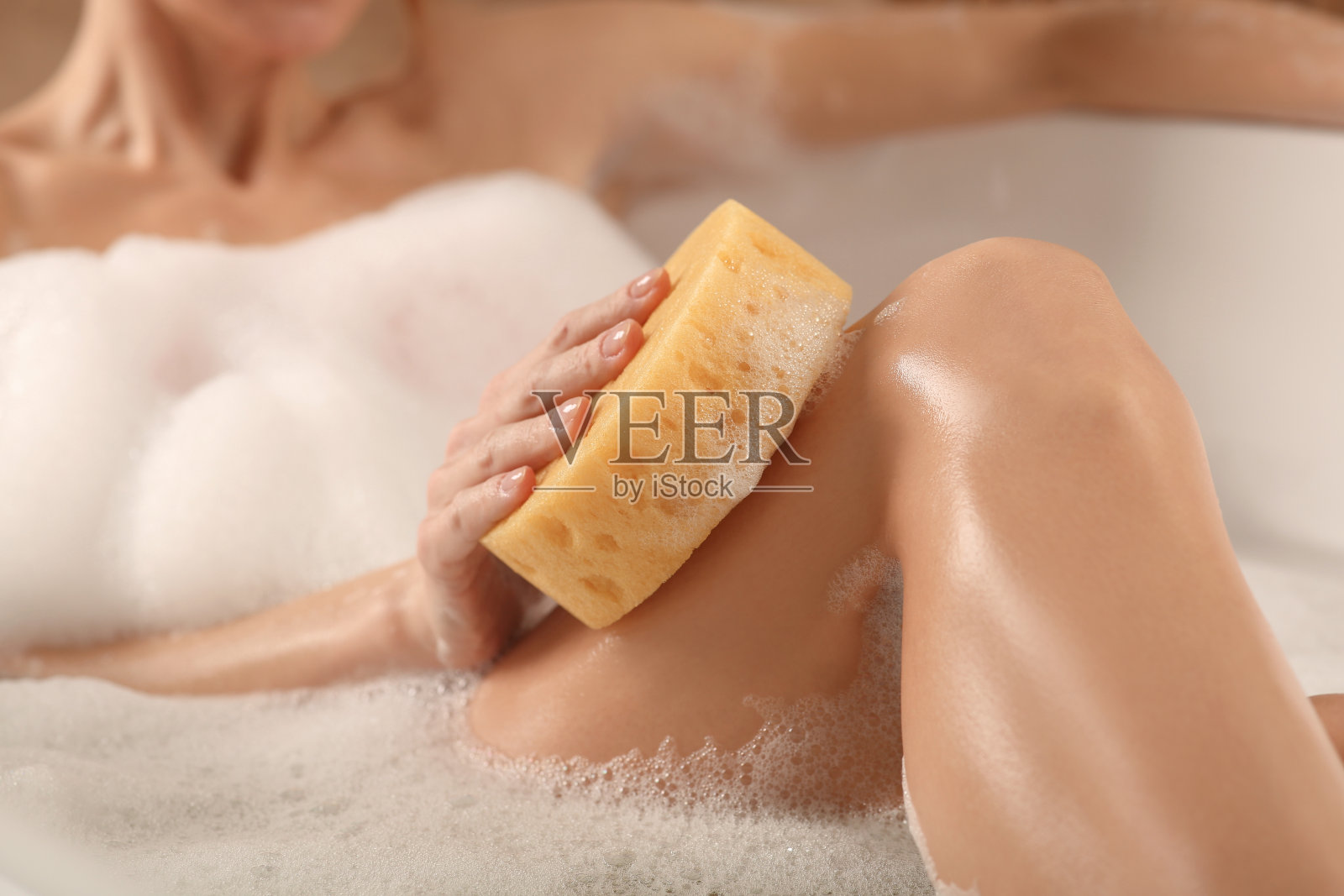 女子洗澡时用海绵擦腿，特写照片摄影图片