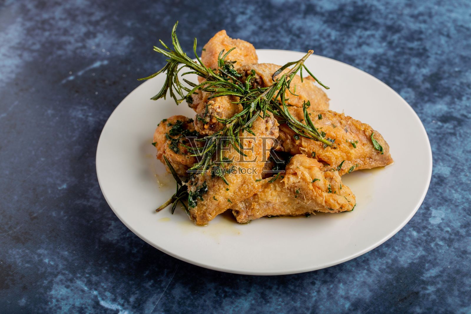 特写一盘美味的炸鸡和干迷迭香放在蓝色的桌子上照片摄影图片