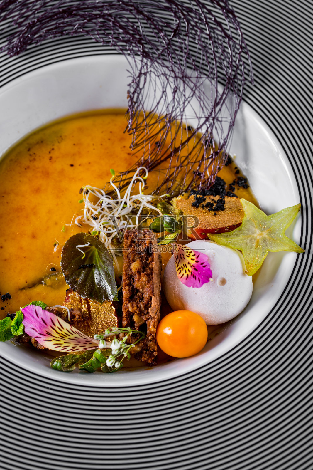 焦糖布丁配一片派，一勺冰淇淋，酸浆，杨桃，嫩芽，花瓣，巧克力线放在盘子里。垂直方向照片摄影图片