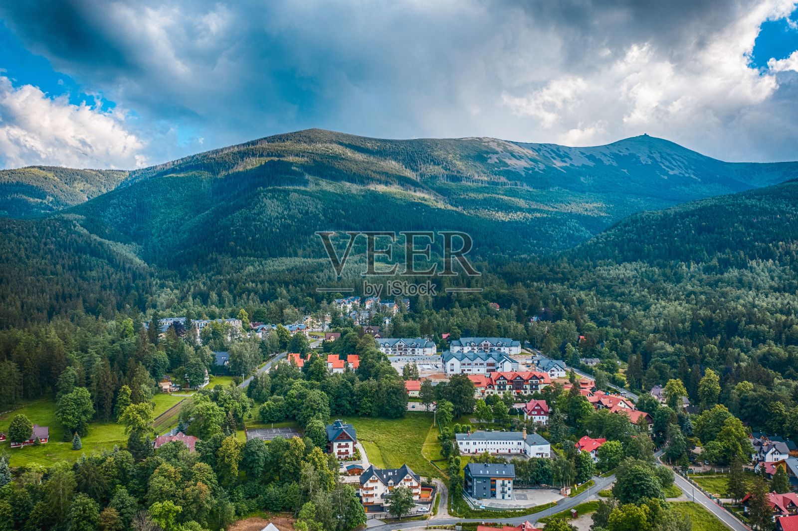 无人机拍摄了在多云的天空下，绿色的卡尔帕兹山脉前美丽的房子和树木照片摄影图片