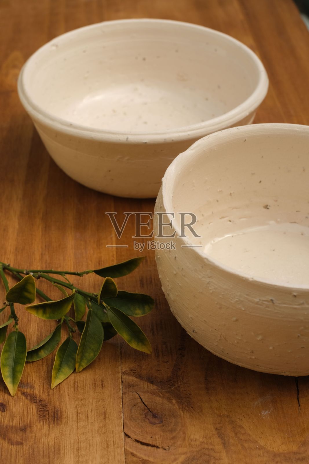 木桌上放着白色的空陶瓷碗和绿叶照片摄影图片