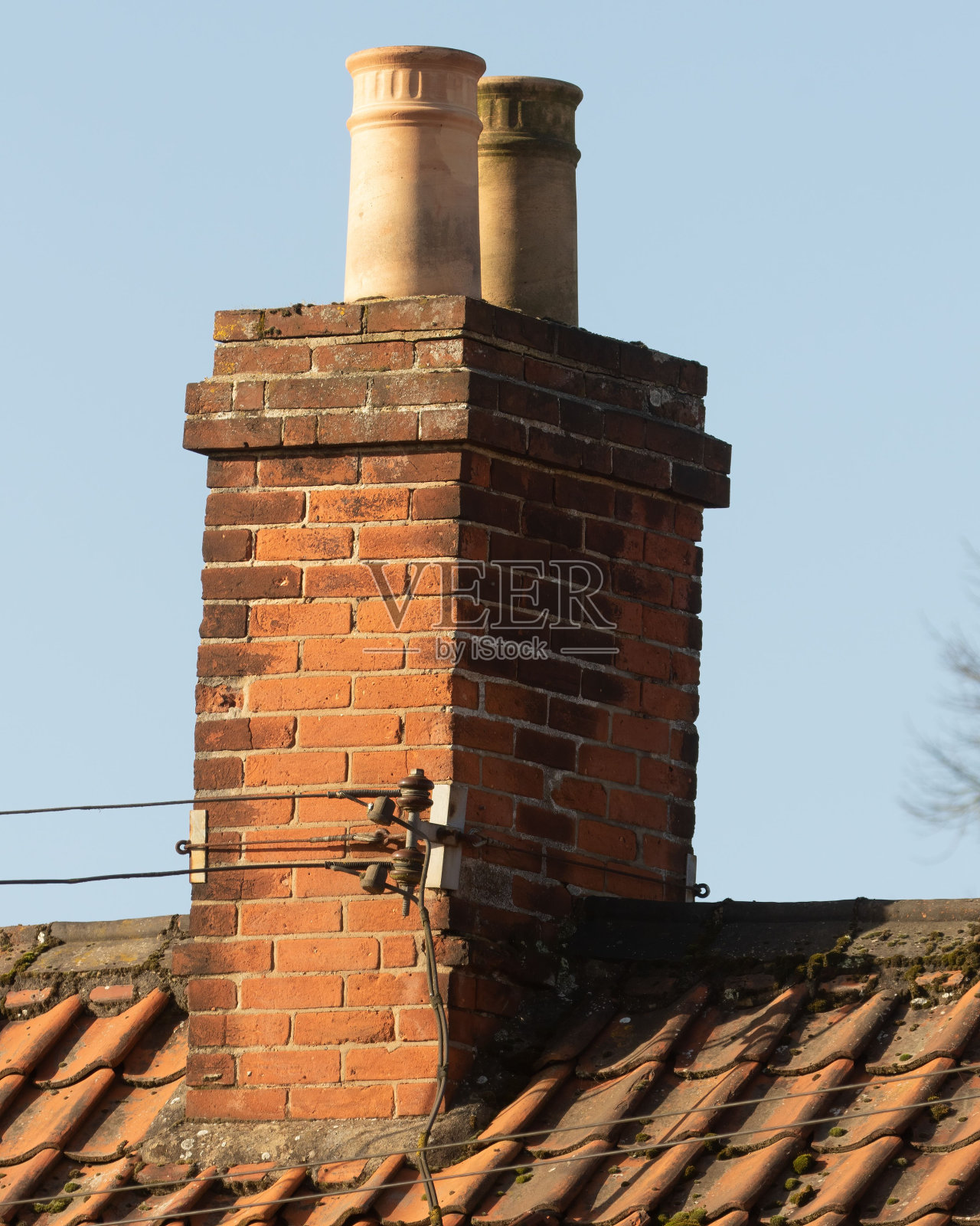 红砖烟囱和屋顶上的两个风化的奶油色烟囱罐，背对着蓝天照片摄影图片