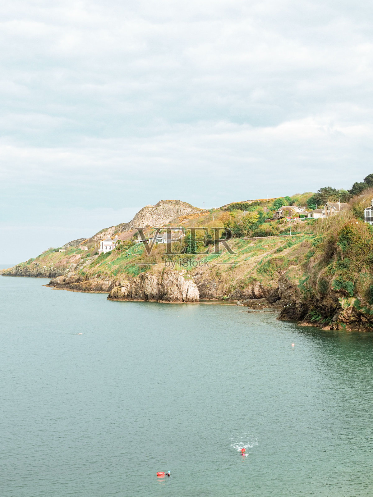 垂直拍摄的房子和绿色灌木生长在悬崖上对着大海在一个阳光灿烂的日子照片摄影图片