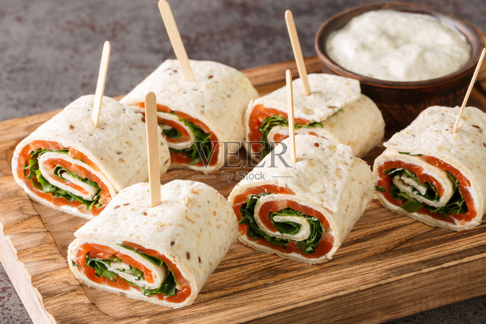 前菜是裹着烟熏鲑鱼片，奶油芝士和香草放在木板上的扁平面包上。水平照片摄影图片