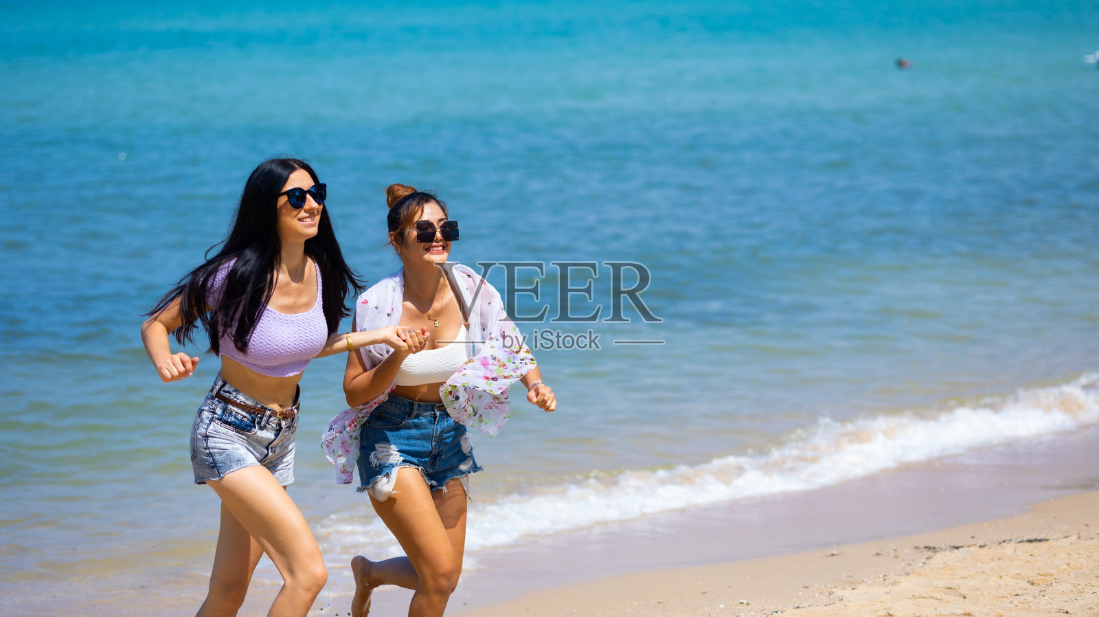 两个美丽的年轻女人在海滩上快乐地奔跑。暑假旅行。朋友牵着手跑步享受生活假期旅行暑假。照片摄影图片