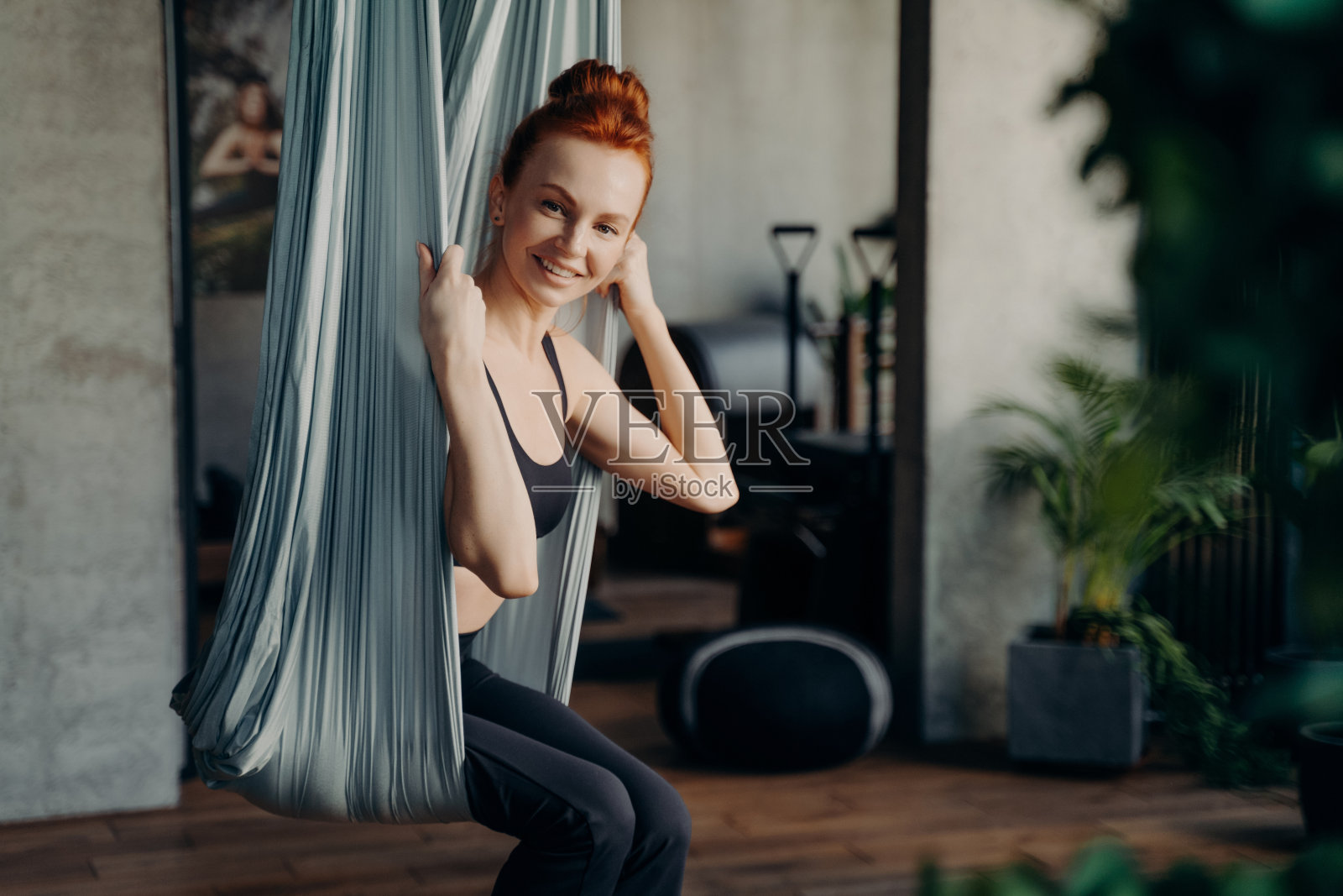 快乐的红头发女人坐在空中瑜伽吊床照片摄影图片