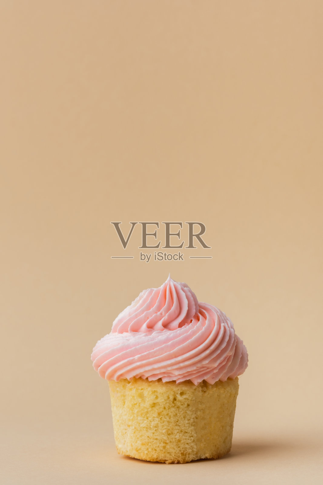 香草纸杯蛋糕的特写，上面有粉红色的奶油奶油。松饼上有奶油芝士糖霜，上面点缀着粉红色心形巧克力。米色背景。情人节快乐照片摄影图片