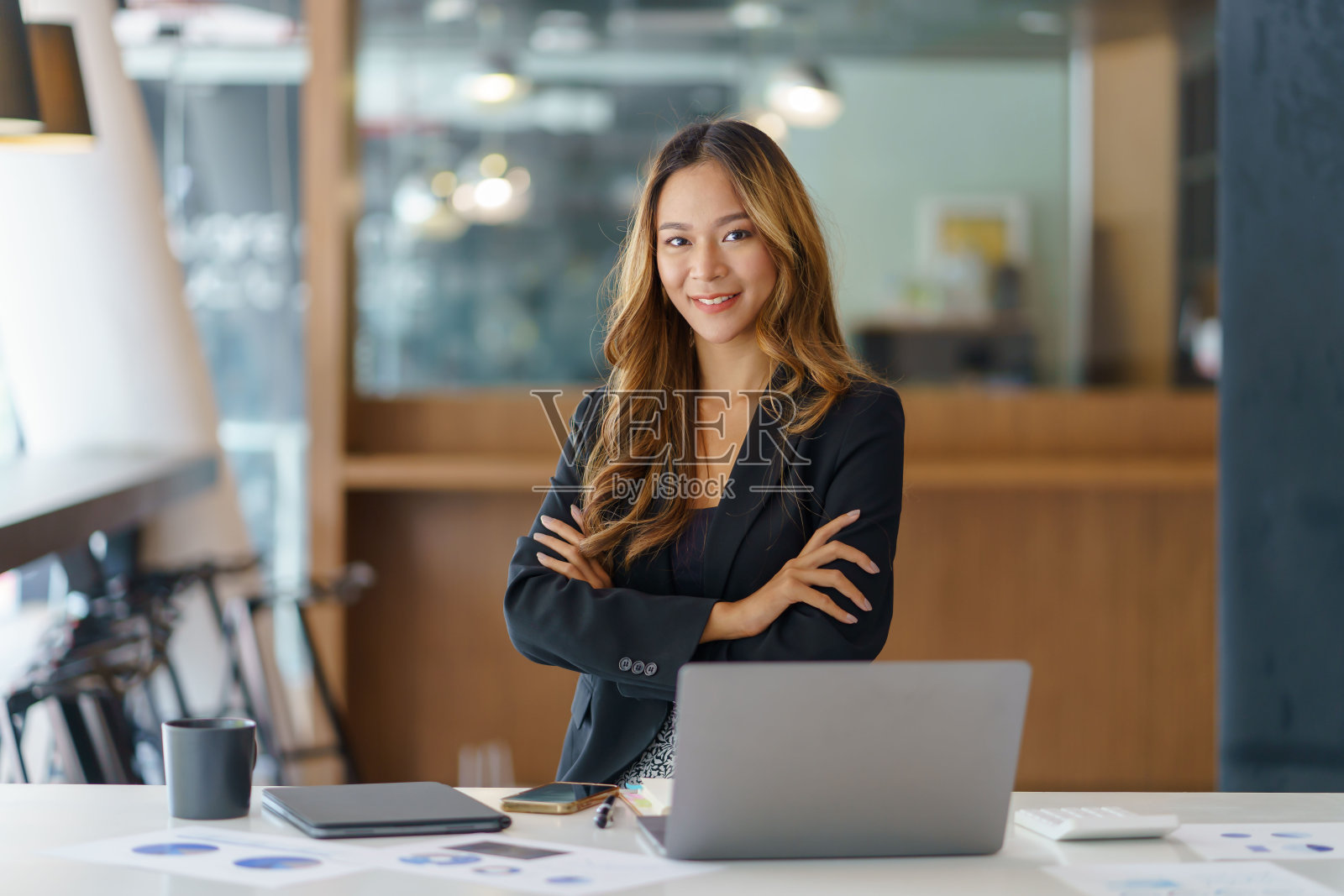 美丽的微笑年轻的亚洲女商人坐在手臂交叉看着相机在办公室。照片摄影图片