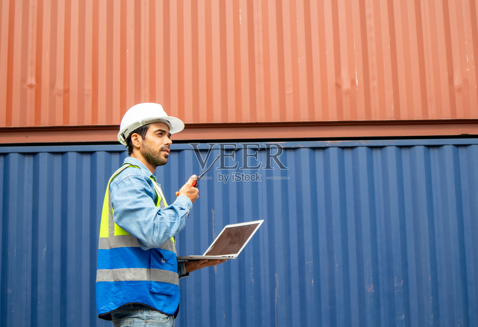 集装箱运输公司的一名男性检查员使用笔记本电脑，通过对讲机报告照片摄影图片